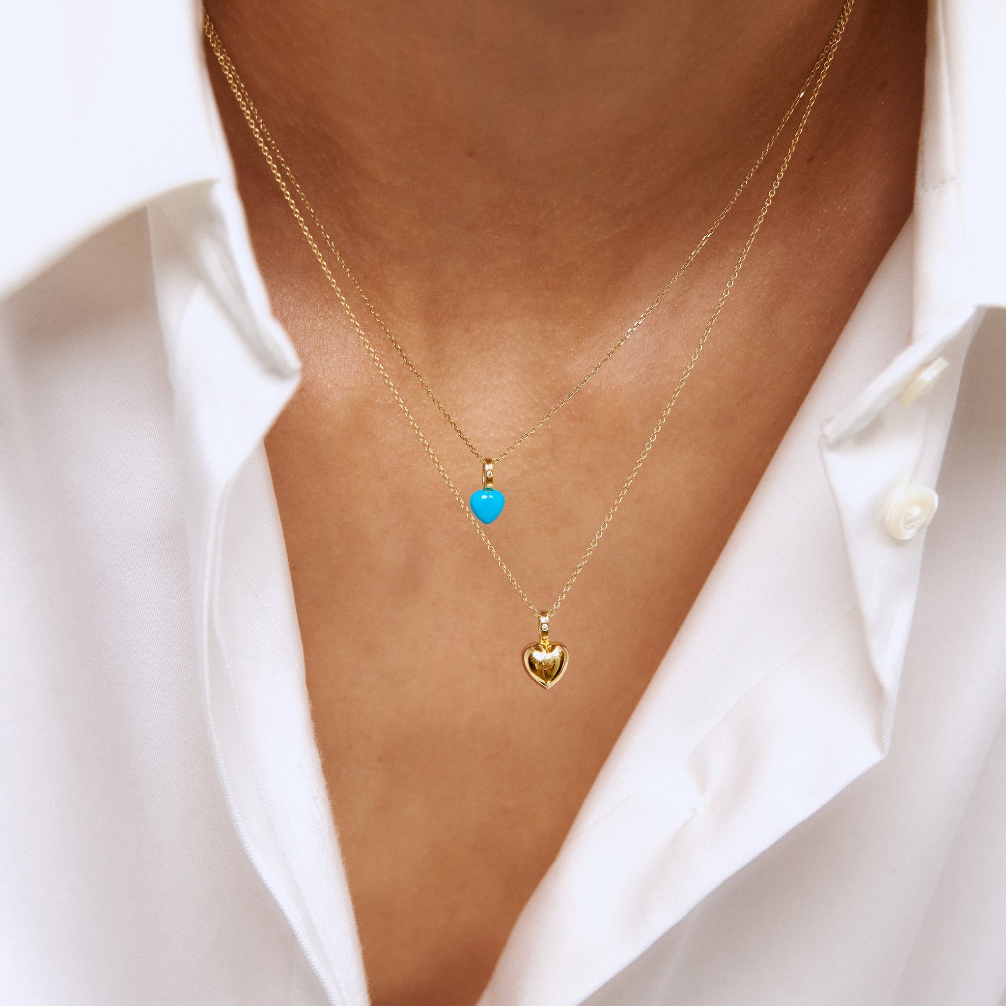 Kvinde i en hvid skjorte, der bærer vores Heart vedhæng sat med en hjerteformet ædelsten i turkis og en diamant samt vores Heart vedhæng i solidt guld sat med en diamant.