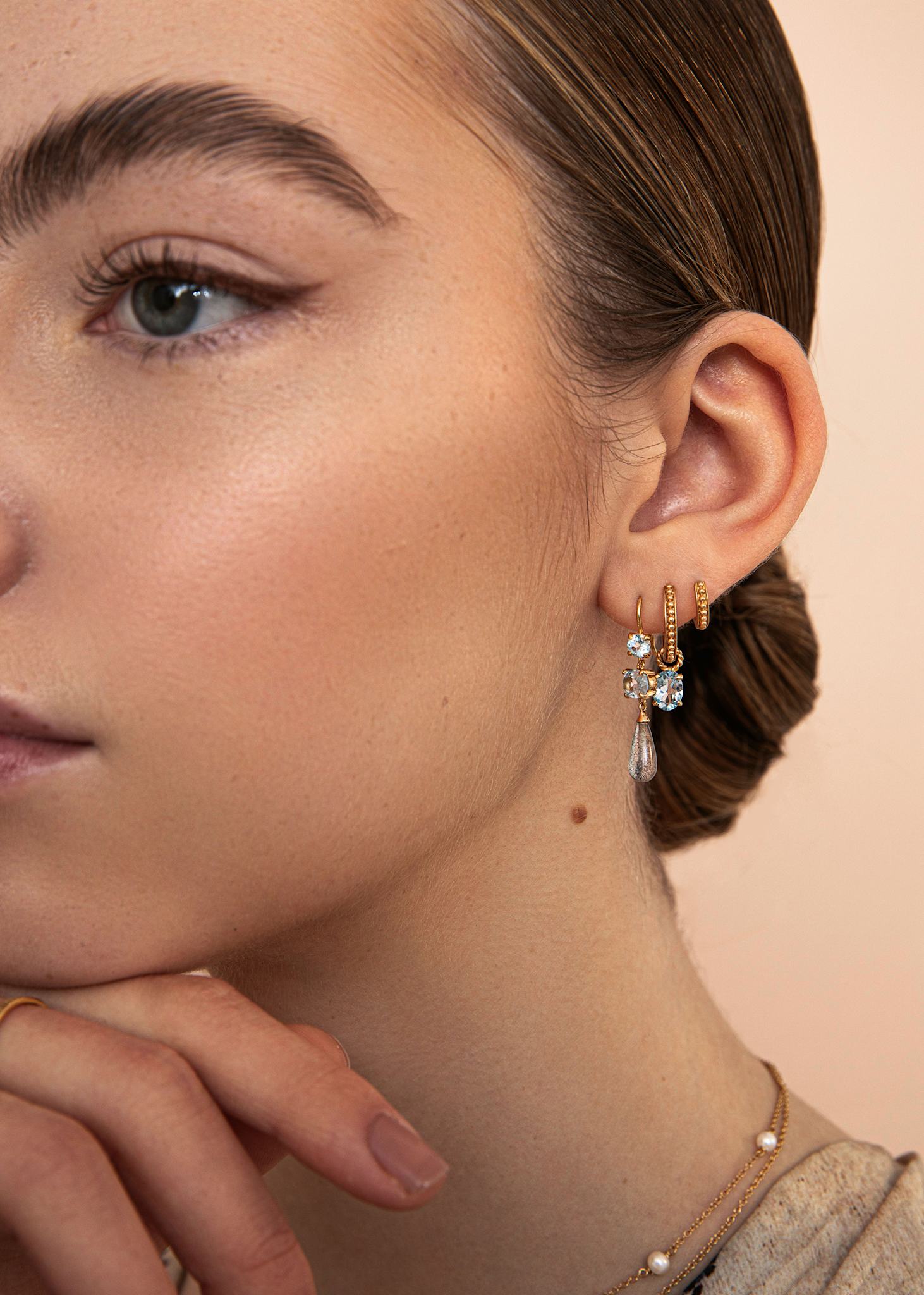 Kvinde med hængeøreringe med dråber af blå topas ædelsten til hoops og charms fra carré jewellery i guld 