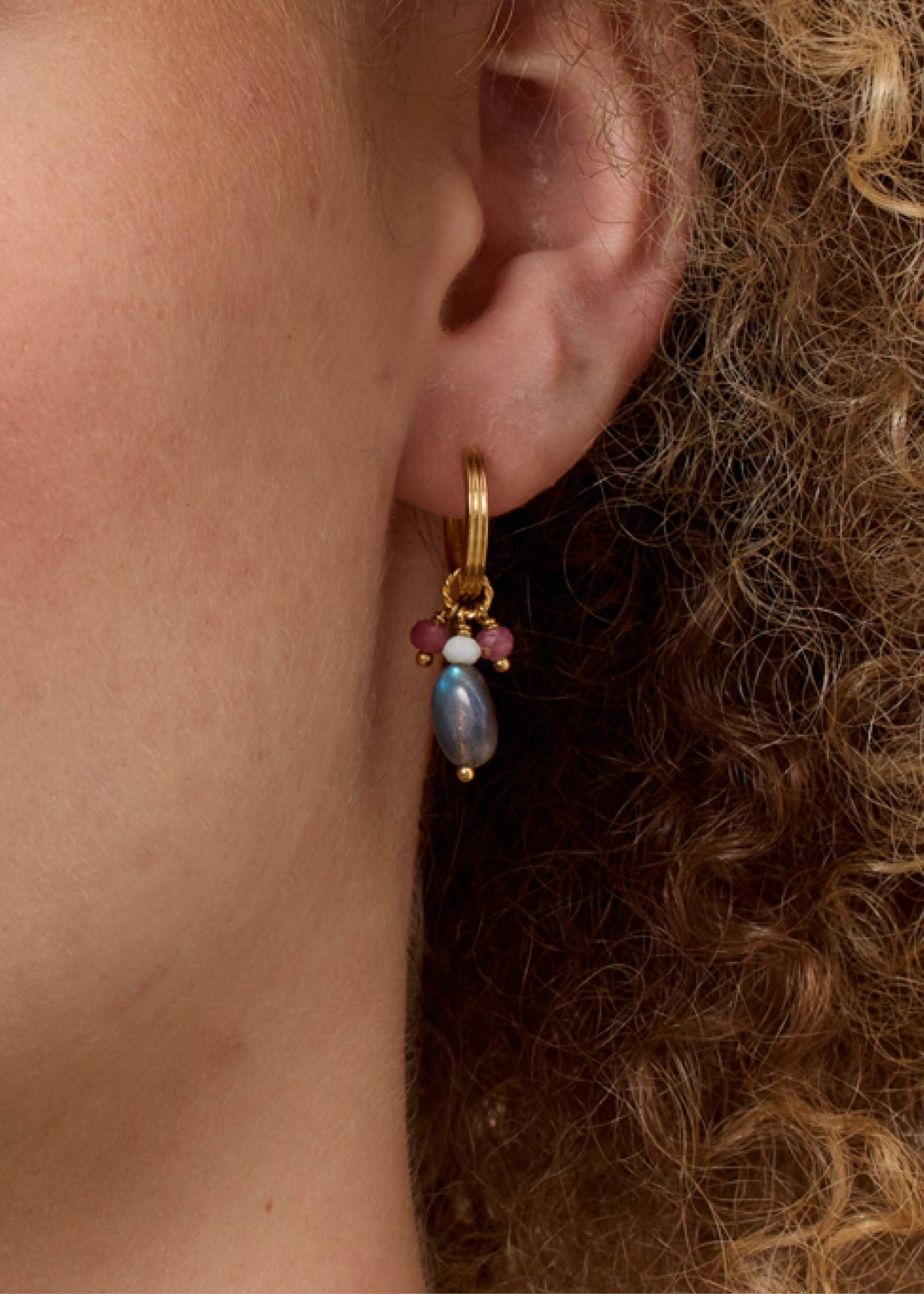 Kvinde med lange øreringe i guld fra Carré Jewellery med pink, grå og grønne ædelsten