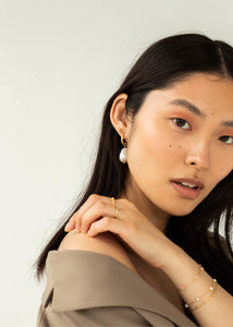Ung kvinde med lille øre sticker fra carré jewellery i guld med blå topas ædelsten og en stor perleørering i guld