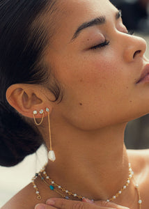 Kvinde med lange hængeøreringe i guld med hvid barok ferskvandsperle og en blå topas ædelsten til mænd og kvinder fra Carré Jewellery 