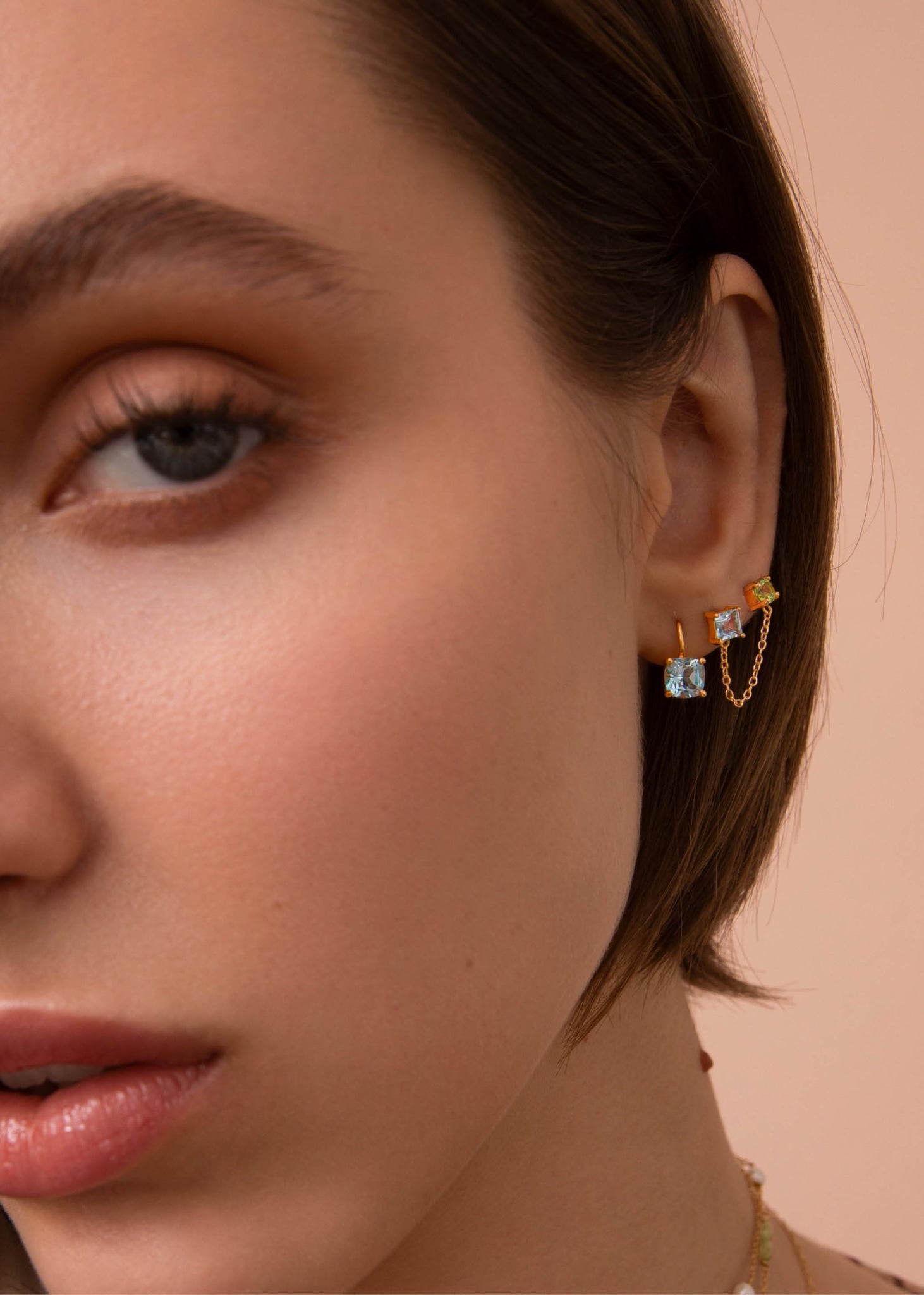 Ung kvinde med guldbelagte øreringe fra carré jewellery med blå topas og grønne peridot ædelsten på udsalg lige nu