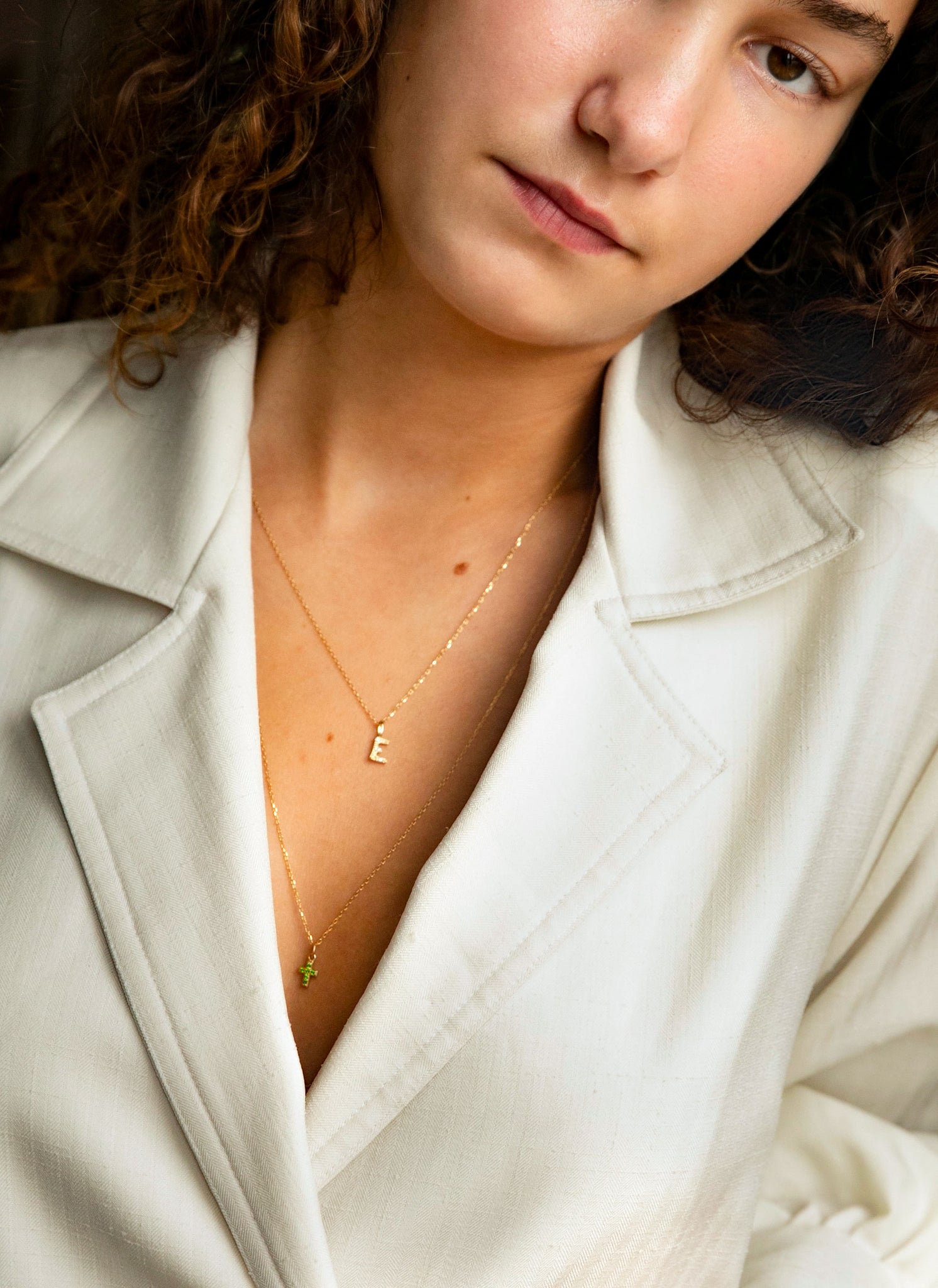 Konfirmand der bærer ægte guld smykker fra carré jewellery til sin konfirmationsgave, hun bærer et kors med grønne sten og et bogstavsvedhæng til halskæder med diamanter i bogstavet E