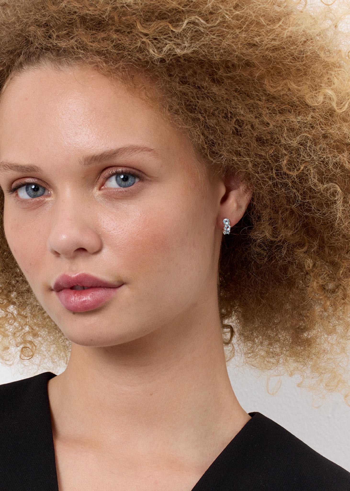 Ung kvinde med huggie hoops fra carré jewellery med blå topas ædelsten i grabbefatninger på tilbud lige nu hos carré Jewellery 