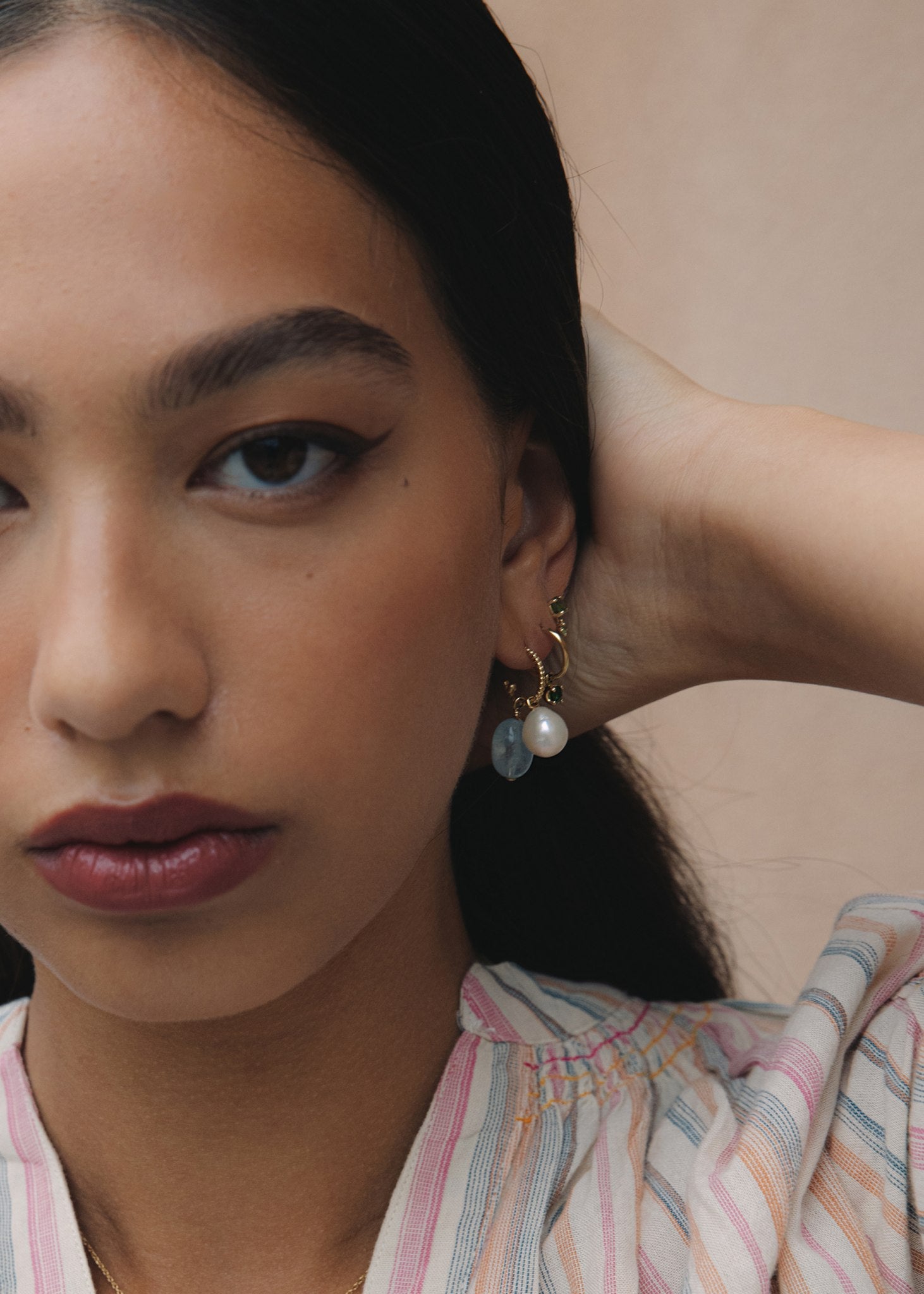 Kvinde med hoops og charms i ægte guld fra carré jewellery sat med hvid ferskvandsperle, grøn turmalin og blå akvamarin ædelsten i cabochonslibning