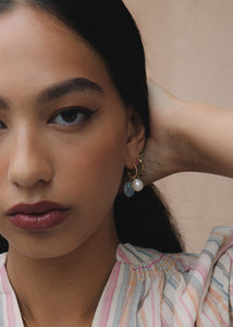 Kvinde med hoops og charms i ægte guld fra carré jewellery sat med hvid ferskvandsperle, grøn turmalin og blå akvamarin ædelsten i cabochonslibning