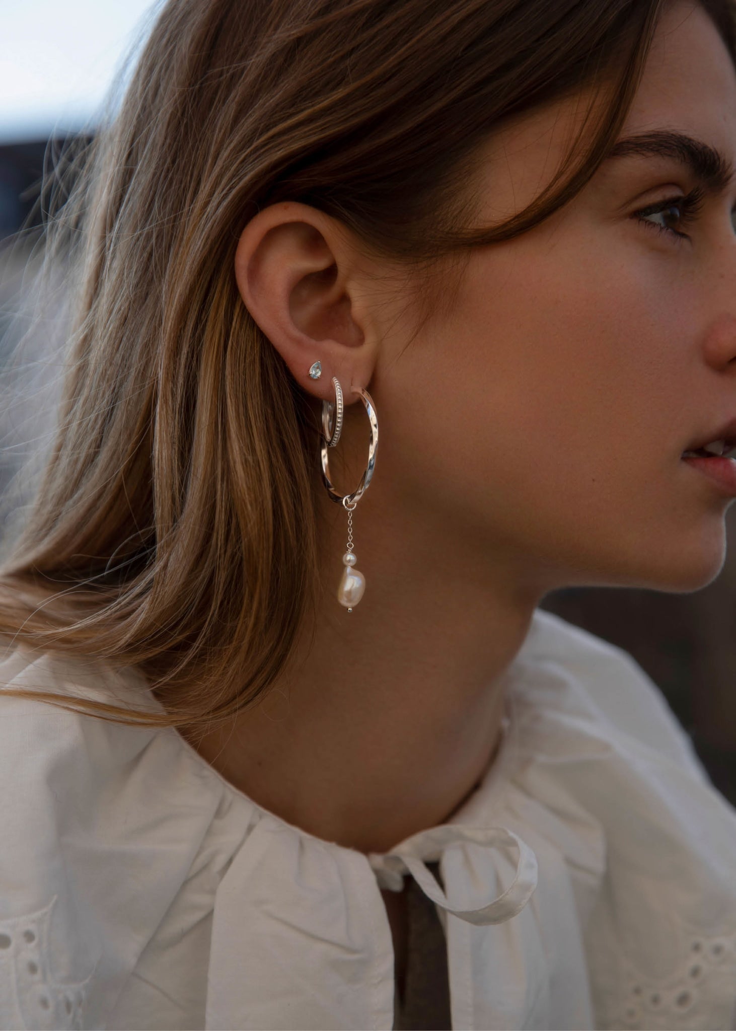 Kvinde med store hoops i sølv med snoet design til mænd og kvinder med et lille ferskvandsperle charm til øreringe