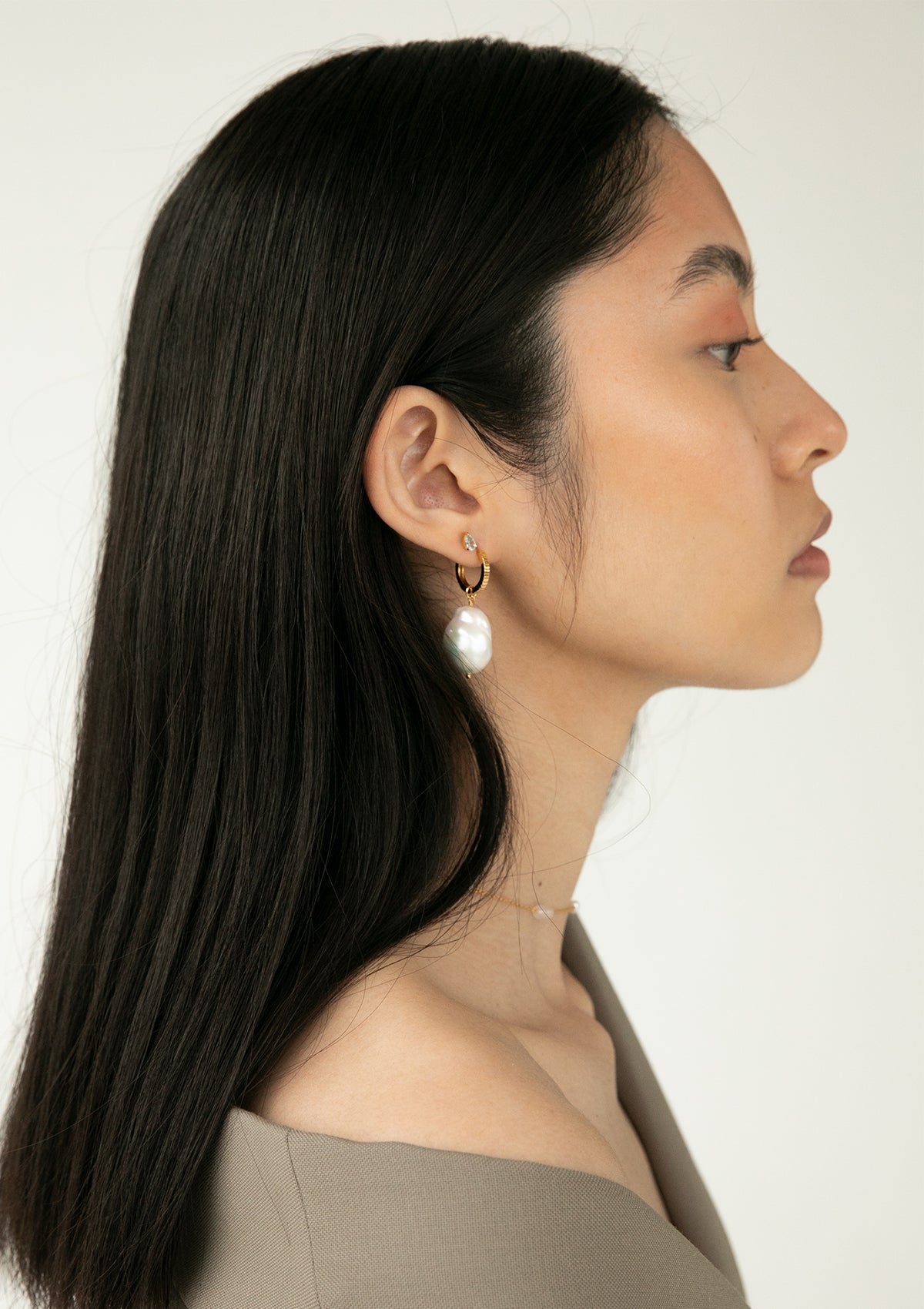 Kvinde med guldbelagte smykker fra Carré. Hun bærer en twist hoop i creol stil med en stor perle charm til hoops.