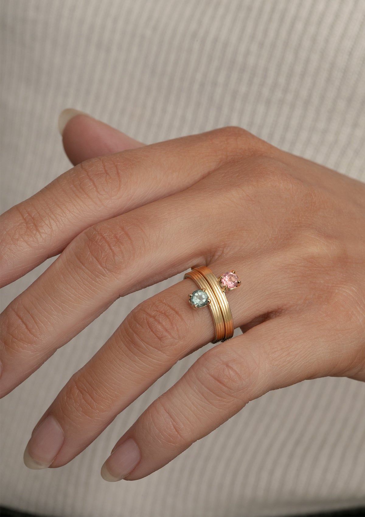 Kvindehånd med to guld smykker i 10 karat guld fra carré. Ringene har en pink turmalin og en grøn turmalin